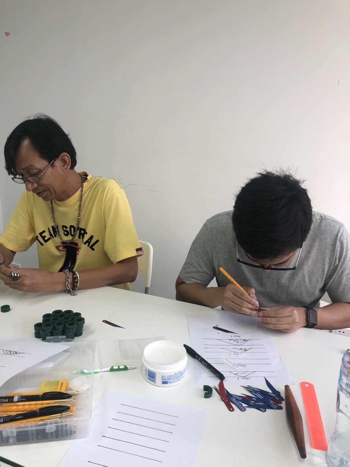 Craftsmen hand-carving green wax ring masters at a work table.